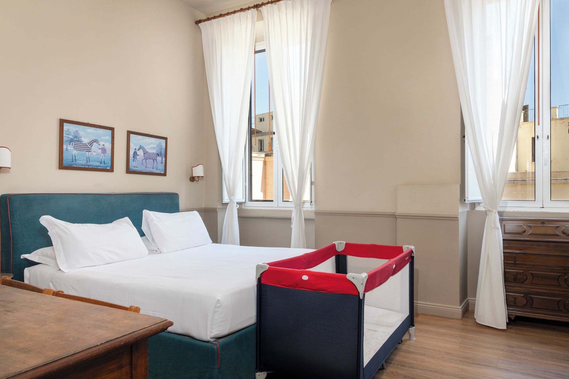 A hotel room with a bed, a desk, a dresser, and a window with curtains.