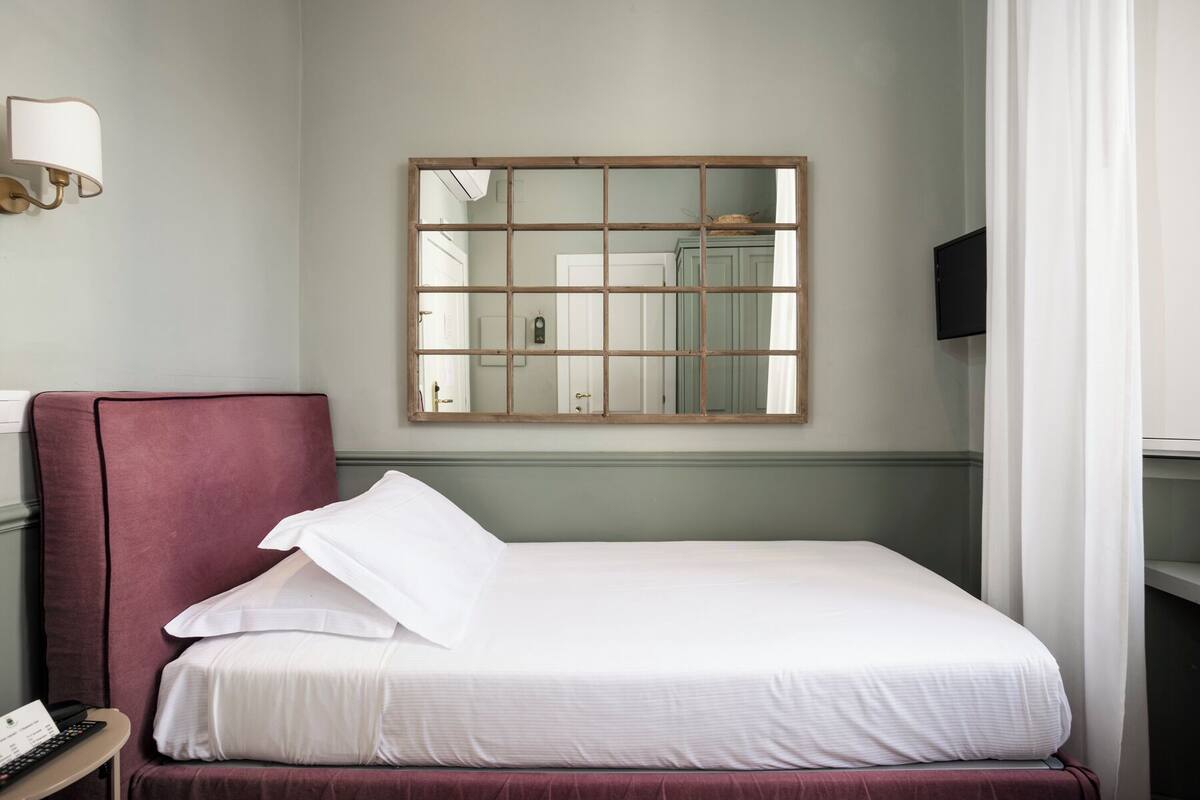 A hotel room with a bed, a bedside table with a lamp, a mirror, and a television.
