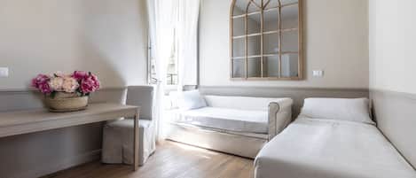 Un dormitorio con cama, un sofá, una mesita con un cesto de flores y un espejo arqueado grande en la pared.
