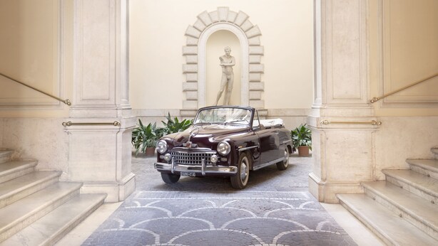 A classic car parked in a grand hallway with marble steps and an arched doorway. - Hotel Donna Francesca (Rome)