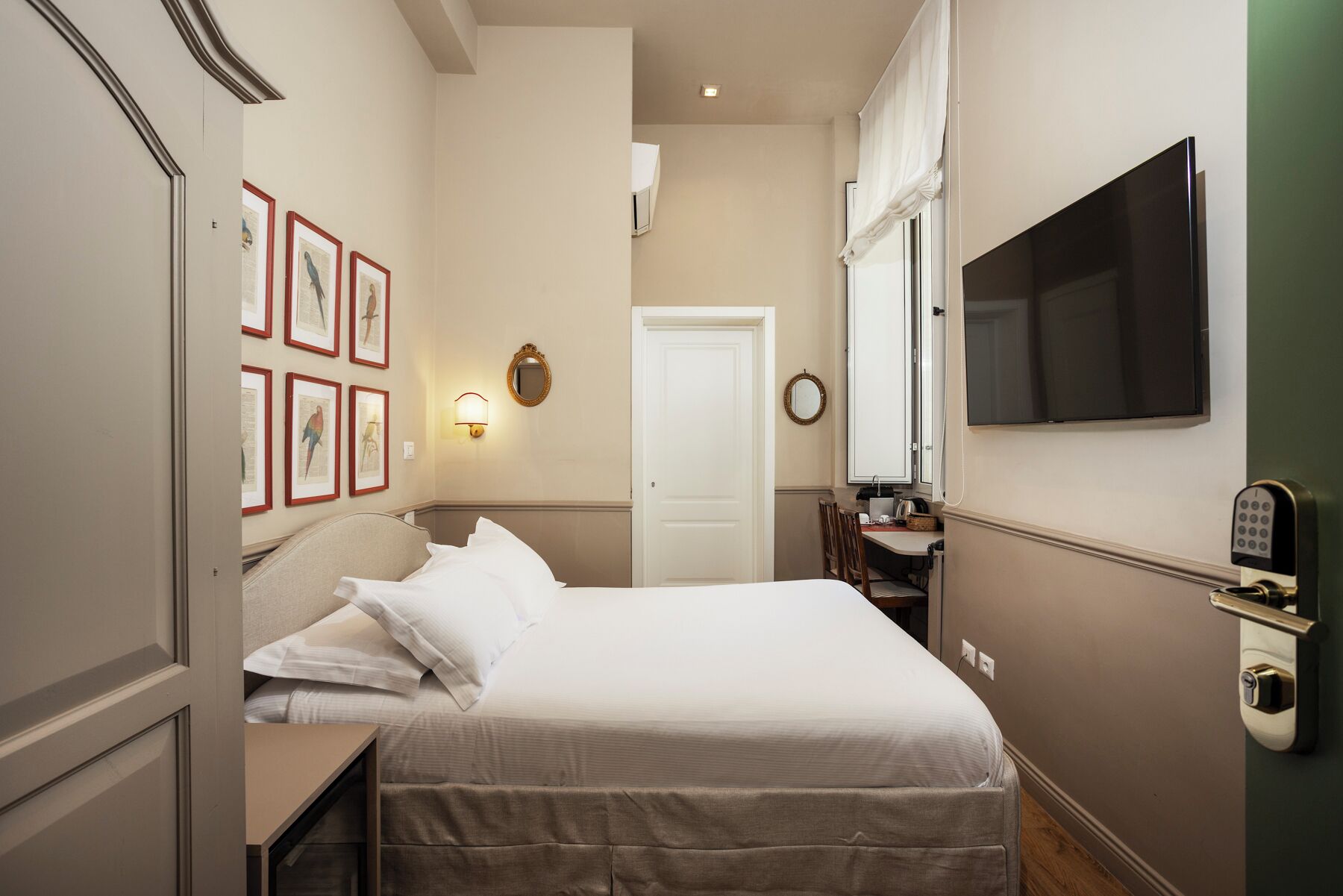 Una habitación de hotel con cama, escritorio, televisión, espejo y cuadros en la pared.
