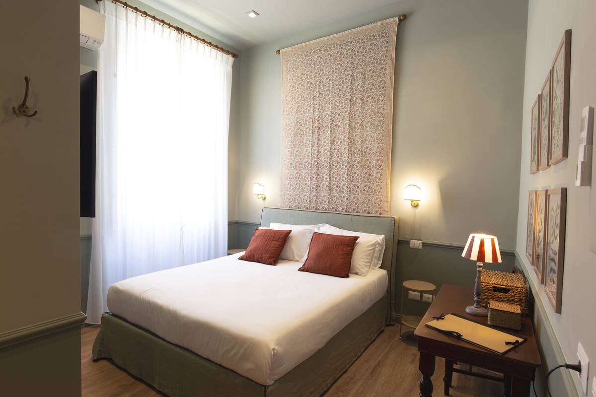 A neatly arranged bedroom with a bed, bedside table, lamp, and wall-mounted artwork.