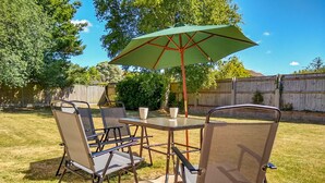 An outdoor patio with a table and chairs, a green umbrella, and a wooden fence in the background. - Sunny Haven (Weymouth)