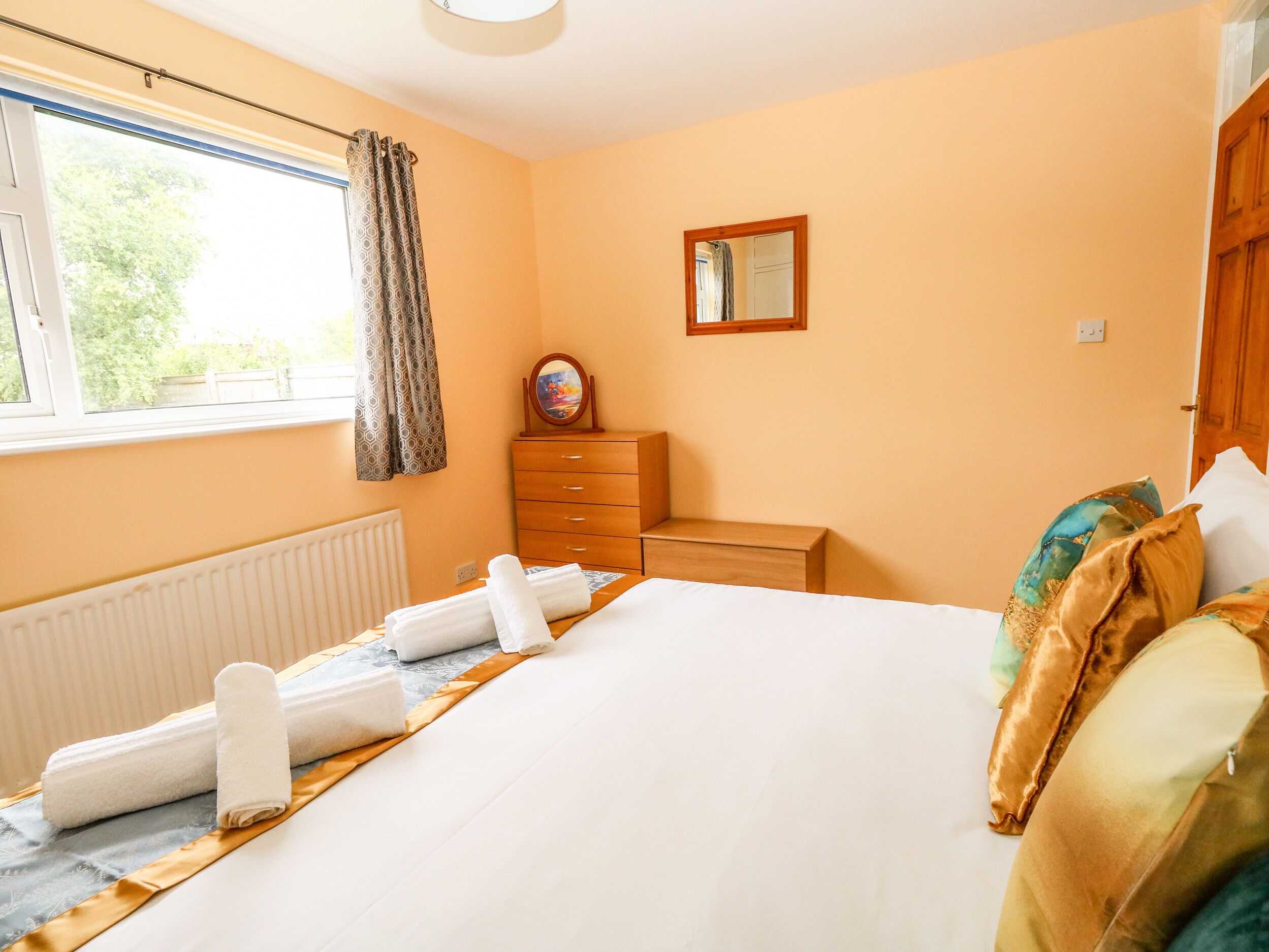 A hotel room with a bed, a dresser, a mirror, and a window with curtains.