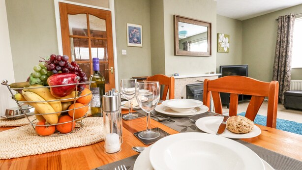 A dining table set with plates, cutlery, glasses, and a fruit basket. - Sunny Haven (Weymouth)