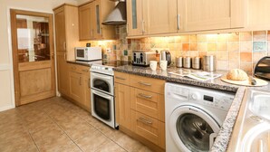 A compact kitchen with wooden cabinets, a microwave, a toaster, a kettle, and a washing machine. - Sunny Haven (Weymouth)