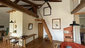 Ein geräumiger Wohnbereich mit Holzbalken, Deckenventilator, Treppe und Esstisch mit Stühlen.