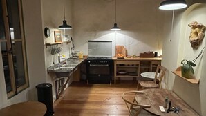Eine kompakte Küche mit Herd, Spüle und Holzboden. Zwei Pendelleuchten, eine Uhr und ein kleiner Topfpflanze sind an der Wand angebracht.
