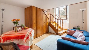 Een woonkamer met een blauwe bank, houten kasten, een trap en een eethoek met een tafel en stoelen.