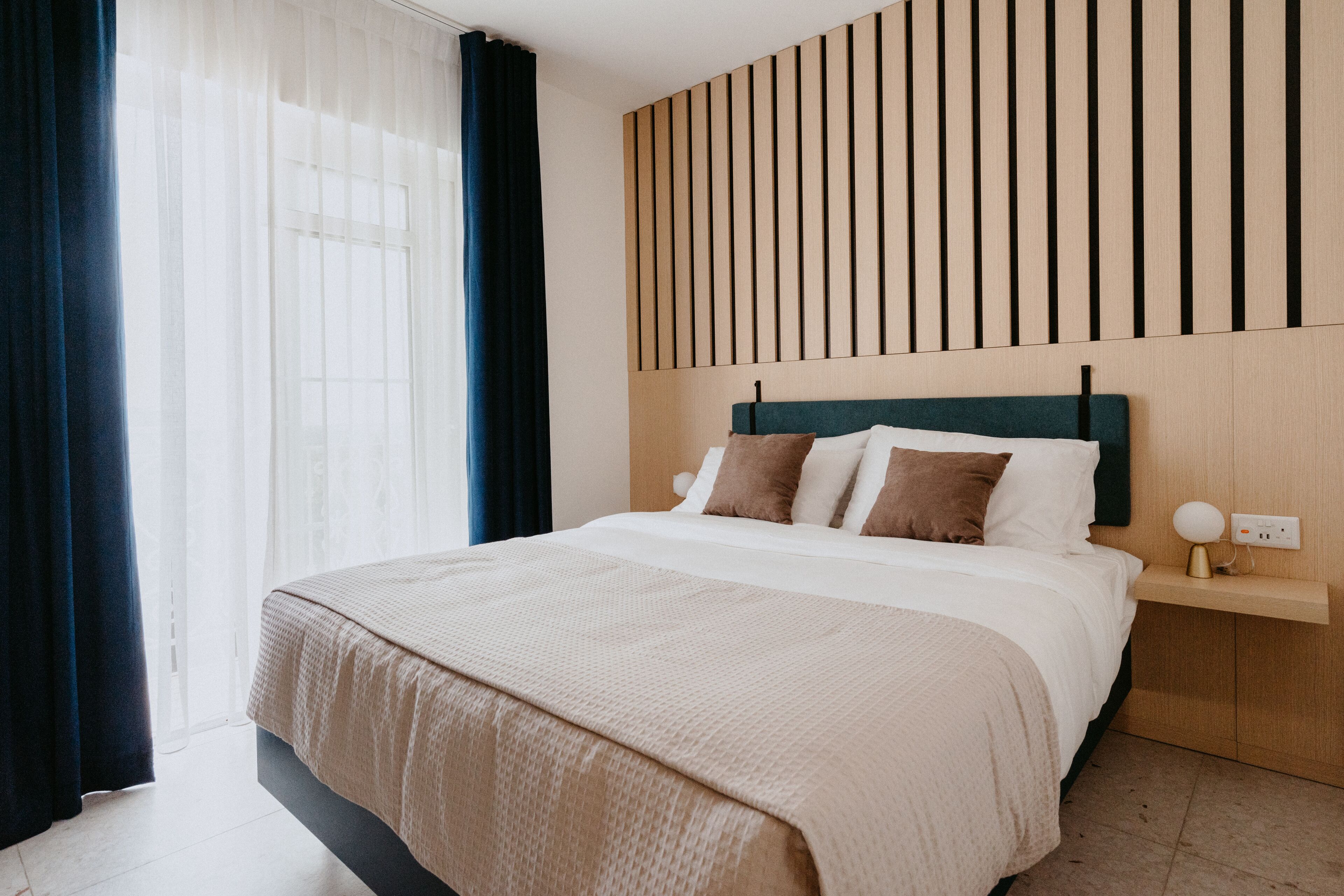 A modern hotel room with a large bed, a wooden headboard, and a bedside table with a lamp.