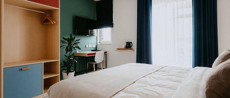 A bedroom with a bed, a desk, a chair, a plant, and a wardrobe.