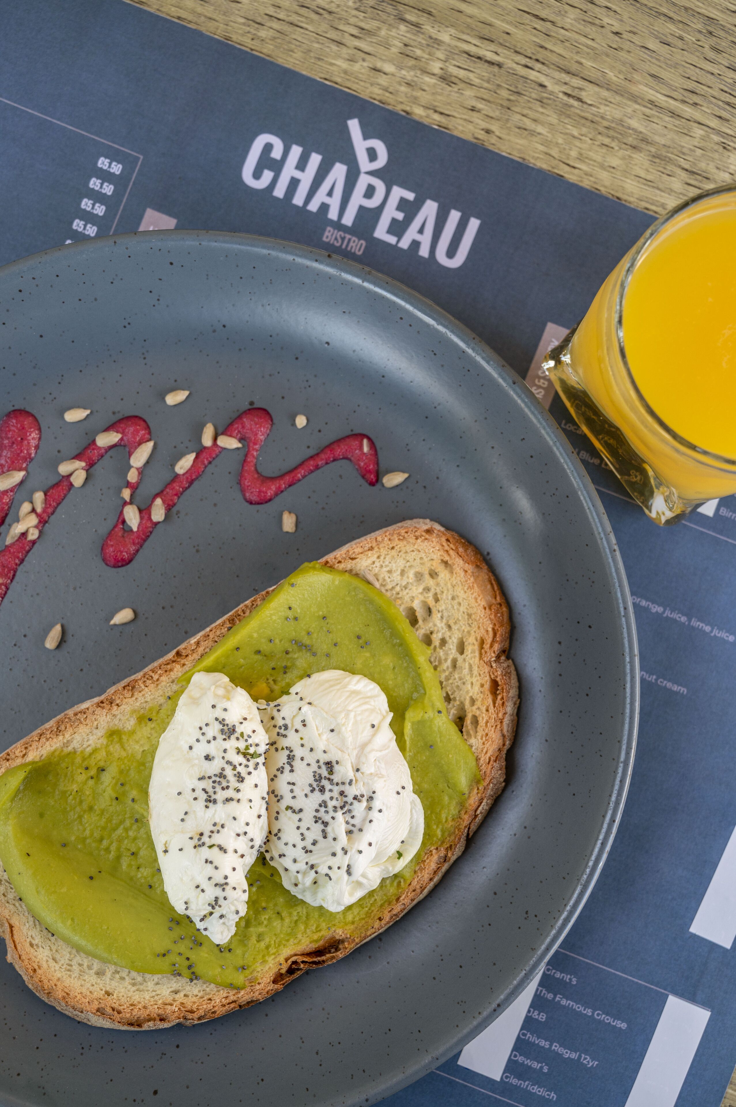 A breakfast plate with toast, avocado, and poached eggs, accompanied by a glass of orange juice and a menu.