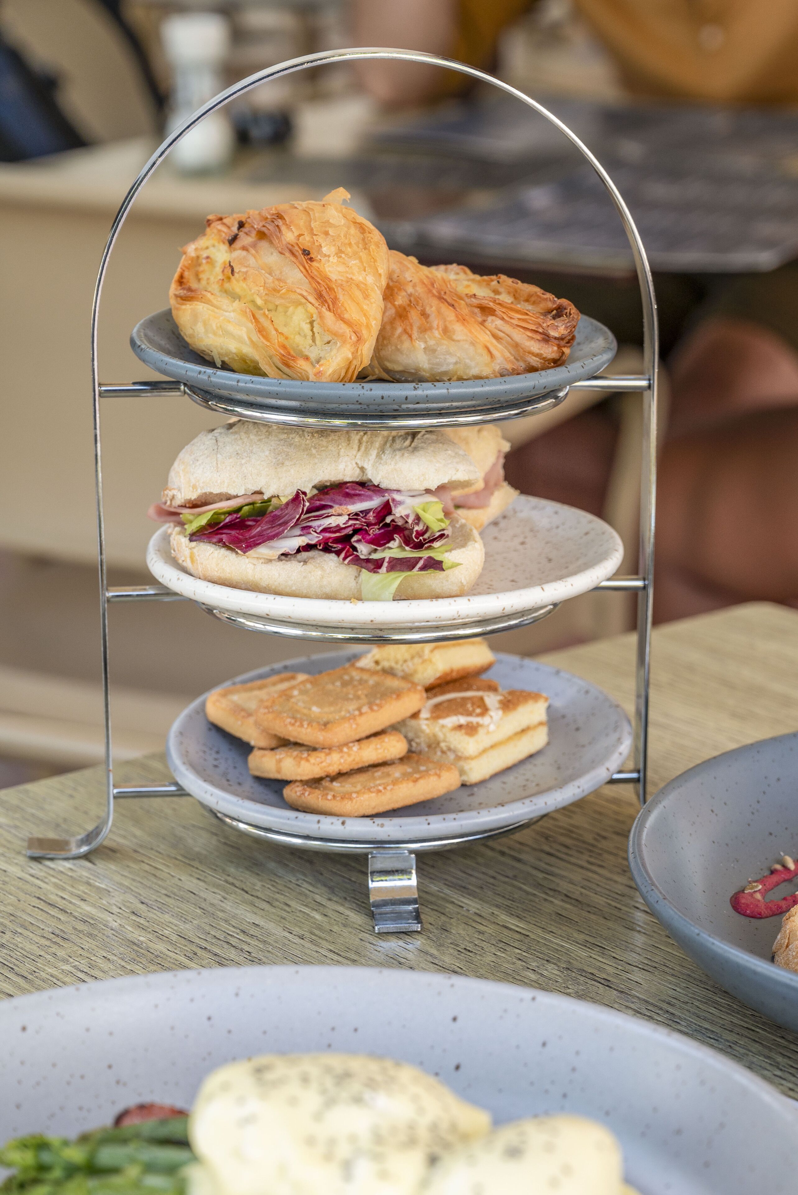 A tiered serving tray with sandwiches, pastries, and biscuits.