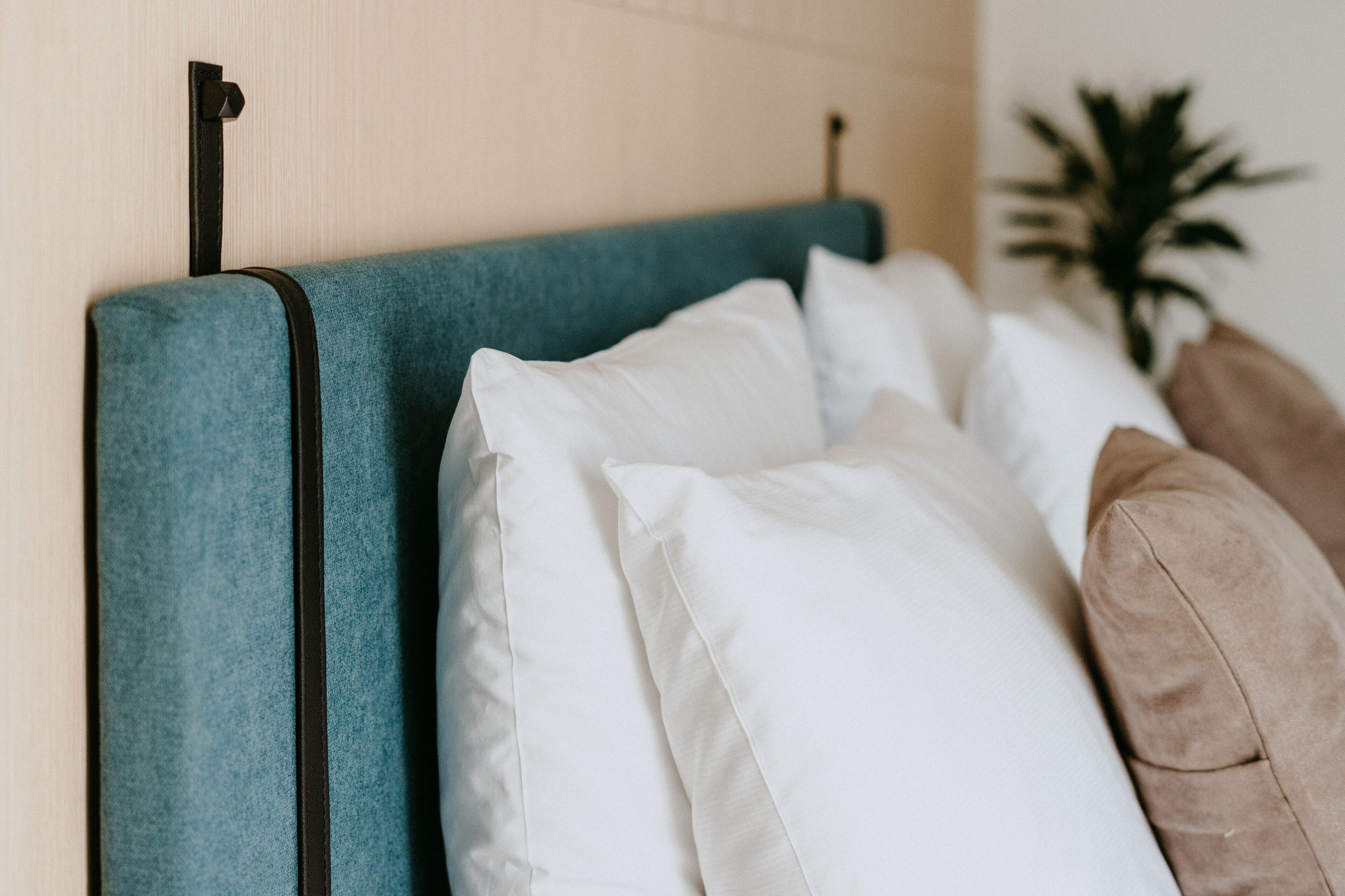 A bed with a teal headboard, white pillows, and a brown pillow.