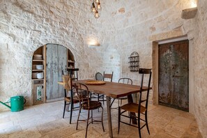 A rustic dining area with a wooden table and chairs, stone walls, and a green watering can.