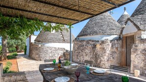 Un espace de restauration en plein air, à l’aspect rustique, avec une table en bois dressée pour quatre personnes, entourée de bâtiments en pierre coiffés de toits coniques.