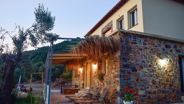 A stone building with a covered patio, outdoor seating, and a view of the surrounding landscape. - Charming 1-bed House in Stafylos (Skopelos)