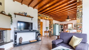 A spacious living room with a fireplace, a large TV, and a comfortable sofa. - Charming 1-bed House in Stafylos (Skopelos)