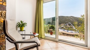 A balcony with a cushioned chair, a small table, and potted plants. - Charming 1-bed House in Stafylos (Skopelos)