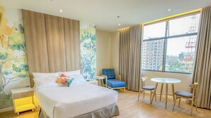 A modern hotel room with a large bed, a small table, two chairs, a blue armchair, and a large window offering a city view. - Harolds Hotel Quezon City (Quezon City)