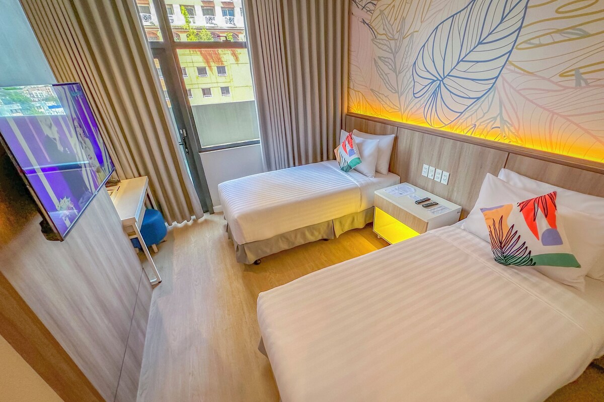 A hotel room with two beds, a TV, a desk, and a window with curtains.