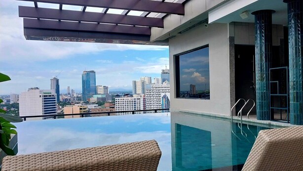 An infinity pool with a city view, a covered seating area, and a glass partition with a view. - Harolds Hotel Quezon City (Quezon City)