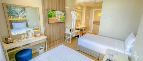 A hotel room with two beds, a desk, a chair, a TV, a mirror, and an air conditioning unit.