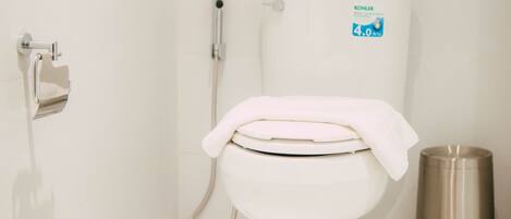A modern bathroom with a toilet, a toilet paper holder, a bidet, and a trash can.