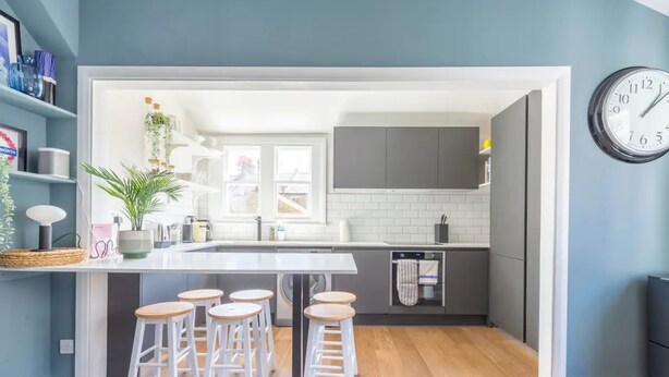 A modern kitchen with a central island, bar stools, and a clock on the wall. - Luxuriously Designed 3 Bedroom Apartment in Clapham (London)