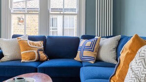 A blue sofa with patterned cushions, a coffee table, and a window with a view of a brick building. - Luxuriously Designed 3 Bedroom Apartment in Clapham (London)
