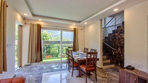 Un comedor con mesa y sillas, una escalera y vistas al exterior con vegetación.
