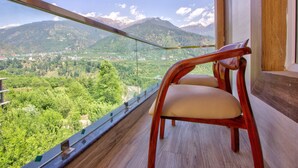 Un balcón con una silla de madera, con vistas a un paisaje montañoso y un pueblo en la falda de la montaña.