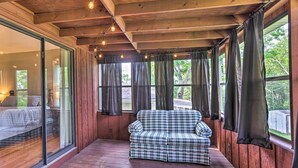 Ein gemütliches Zimmer mit einer karierten Couch, Holzbalkendecke und großen Fenstern mit Vorhängen.