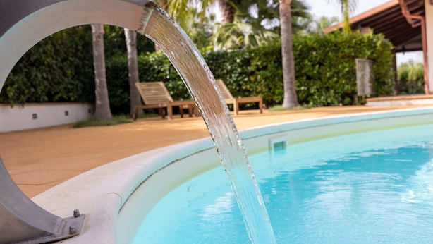 A pool with a water feature, surrounded by palm trees and lounge chairs.