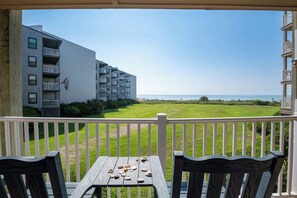 A balcony with a view of a grassy area and a building with multiple balconies.