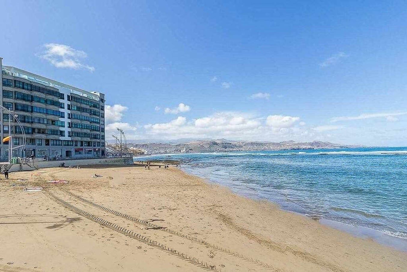 Une plage avec un bâtiment sur la gauche, un ciel dégagé et une mer calme.