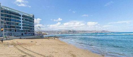 Une plage avec un bâtiment sur la gauche, un ciel dégagé et une mer calme.
