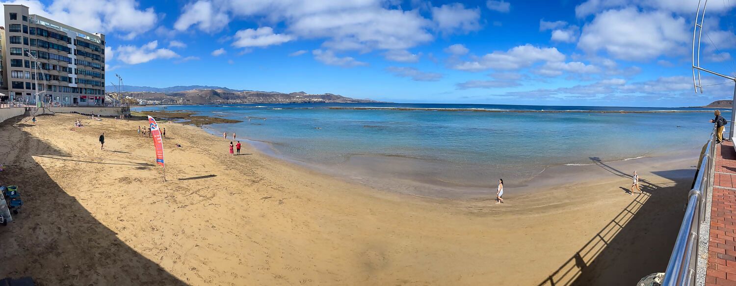 Une plage avec un bâtiment en arrière-plan, un ciel dégagé et une eau calme.