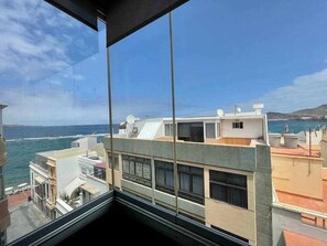 Blick aus einem Fenster auf eine Küstenlandschaft mit Gebäuden, einem klaren Himmel und dem Ozean.