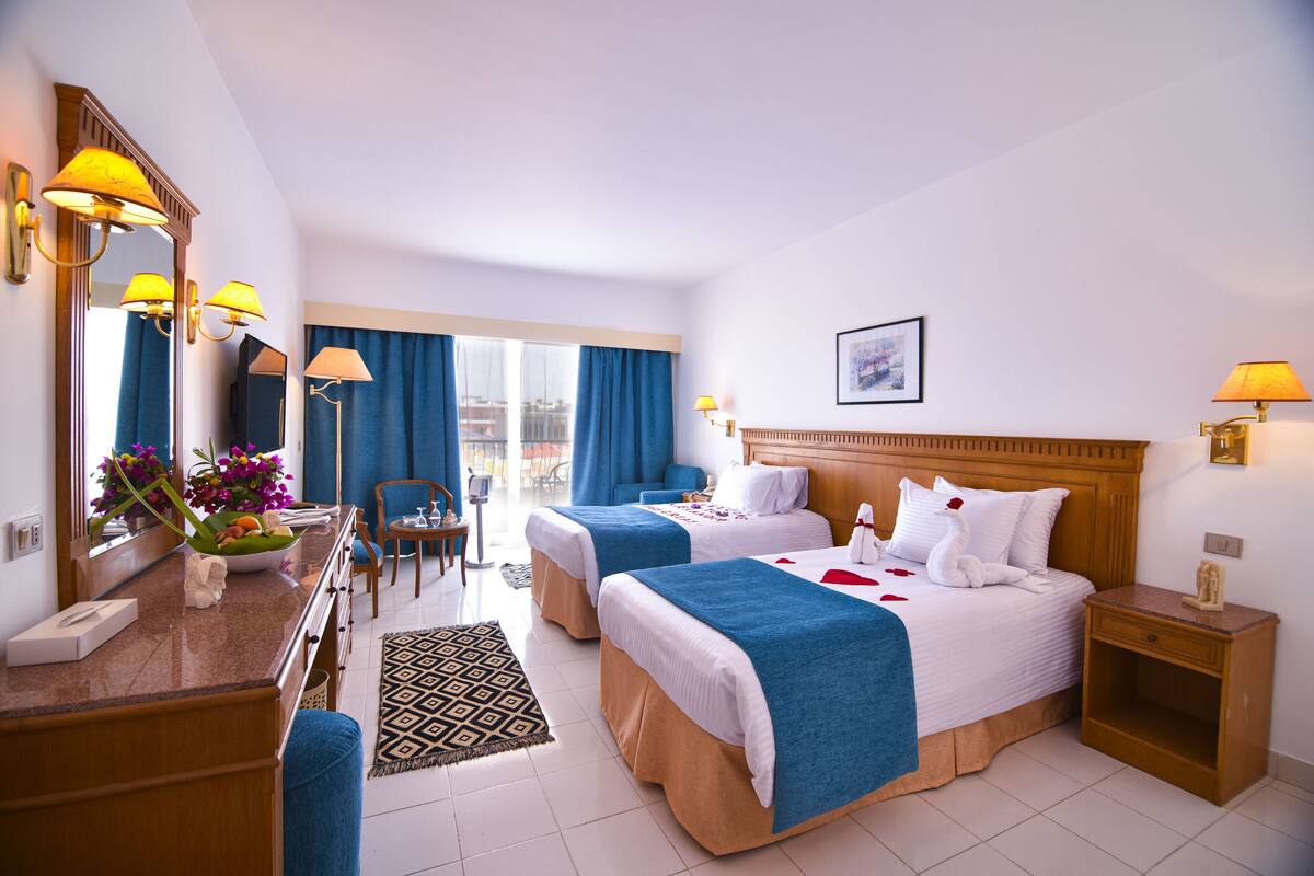 A hotel room with two beds, a desk with a mirror, a chair, and a window with curtains.