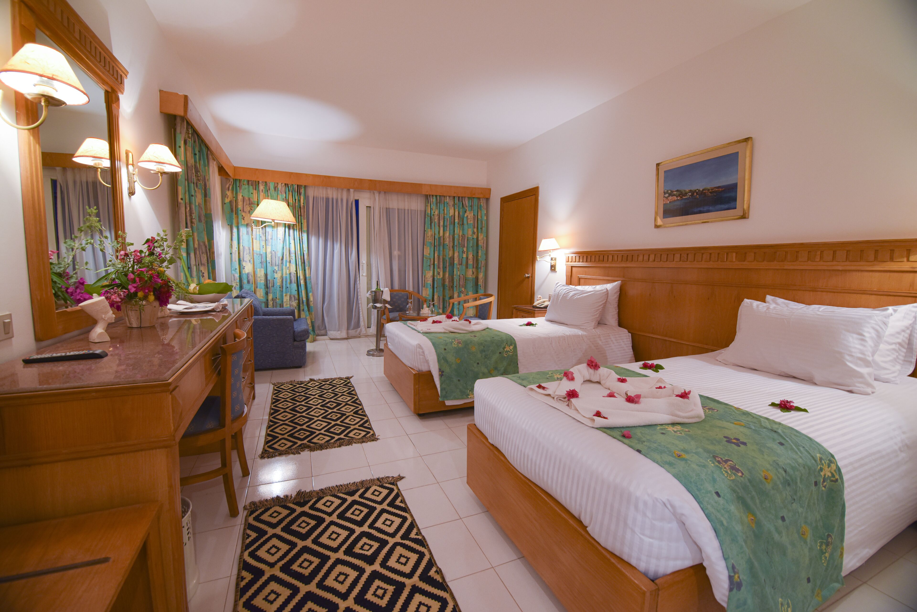 Une chambre d’hôtel avec deux lits, un bureau, une chaise, un miroir et une fenêtre avec des rideaux.