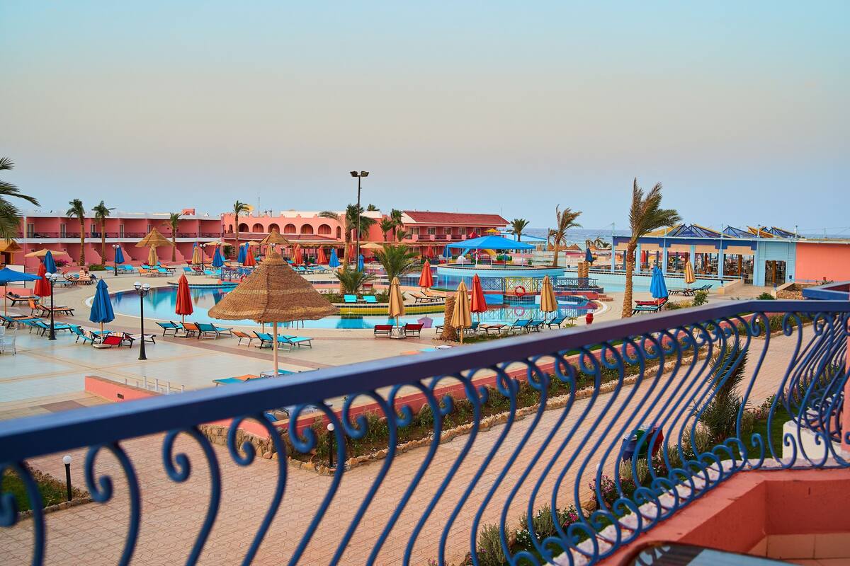 A resort with a swimming pool, lounge chairs, umbrellas, and a building with a red facade.