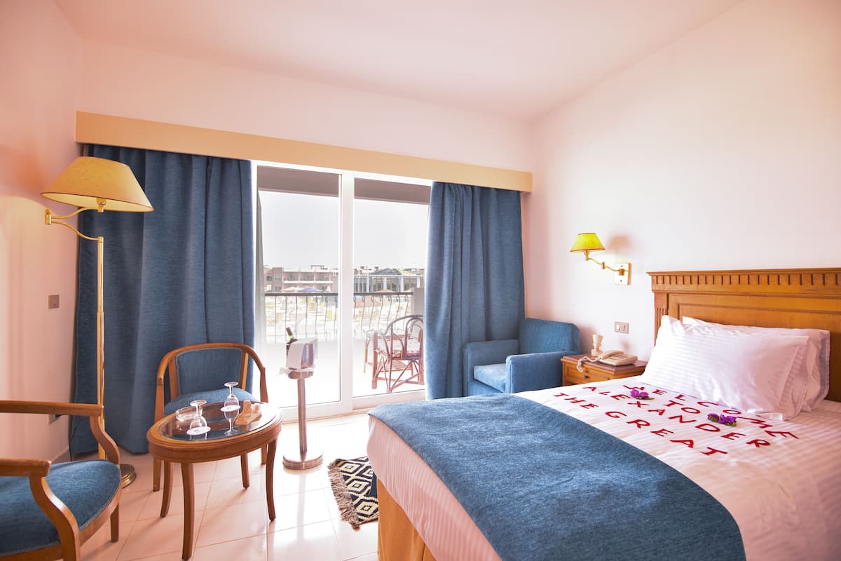 A hotel room with a bed, a chair, a table with glasses, and a view of the outside.
