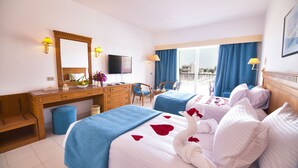 A hotel room with two beds, a desk, a chair, a television, and a balcony with blue curtains. - MG Alexander The Great (Marsa Alam)