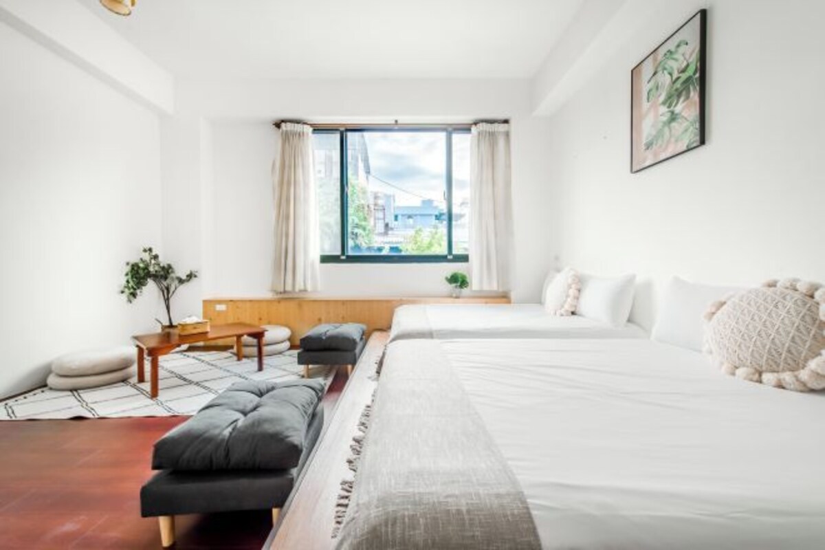 A modern hotel room with a large bed, a sofa, a small table, and a window with curtains.