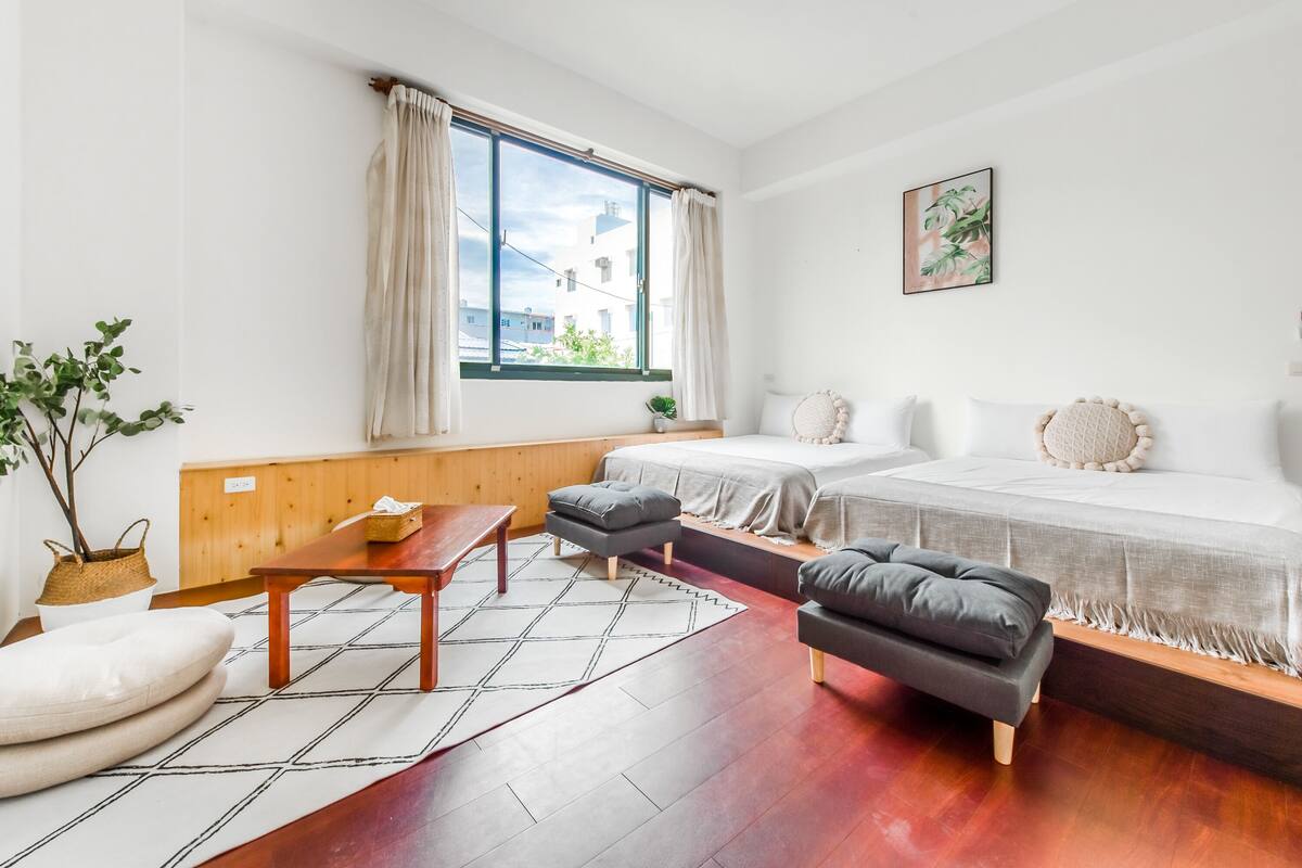 Habitació moderna i ben il·luminada amb terra de fusta, un llit, un sofà, una taula petita i una banca.