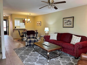 A living room with a red sofa, a plaid armchair, a coffee table, a ceiling fan, and a fireplace.