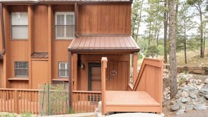 A two-story wooden building with a front porch, a door with a number plaque, and a small wooden bench. - Grisham’s View Condo| Cozy w/Golf Course Views! (Ruidoso)