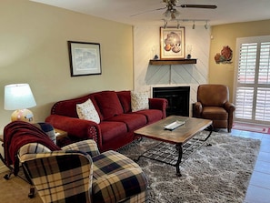 A living room with a red sofa, a plaid armchair, a coffee table, a fireplace, and a ceiling fan.