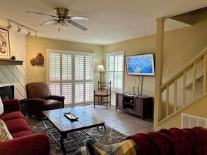 A living room with a fireplace, a ceiling fan, a television, and a staircase. - Golf Course Front Condo | Ruidoso Getaway w/ (Ruidoso)